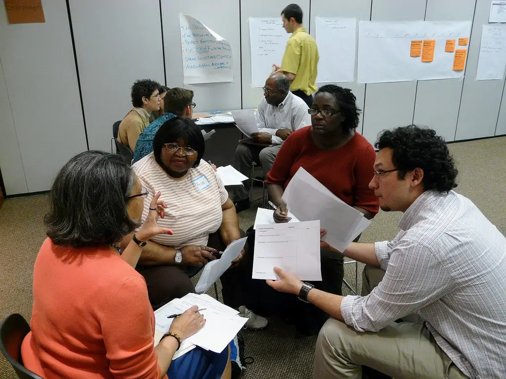 Three people sit in a small circle and discuss issues with paper in hands