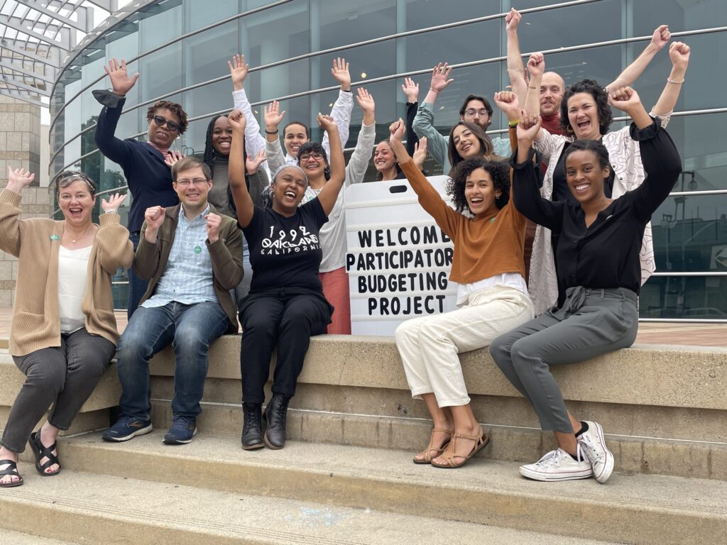 Organization staff with raised hands in celebration, sitting on steps in front of museum