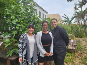 Three people in a row standing in a garden, smiling at camera