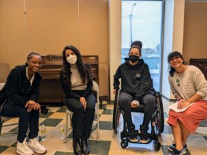 four people sitting in chairs in a room with a tile floor, smiling at camera